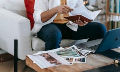 Un designer consulte un carnet, des photographies imprimées et un ordinateur portable.