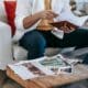 Un designer consulte un carnet, des photographies imprimées et un ordinateur portable.