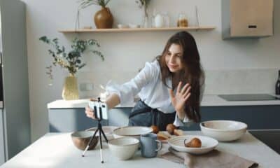 Une créatrice filme une vidéo dans sa cuisine avec un smartphone posé sur un trépied.
