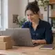 Une personne travaille sur un ordinateur portable, avec deux colis posés sur son bureau.