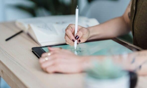 Designer dessinant au stylet sur une tablette posée sur un bureau en bois