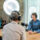 Deux interlocuteurs équipés de casques et de microphones enregistrent un podcast en studio.