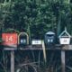 Six boîtes aux lettres numérotées alignées devant une haie