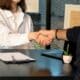 Deux personnes se serrent la main au-dessus d’un bureau avec un ordinateur portable.